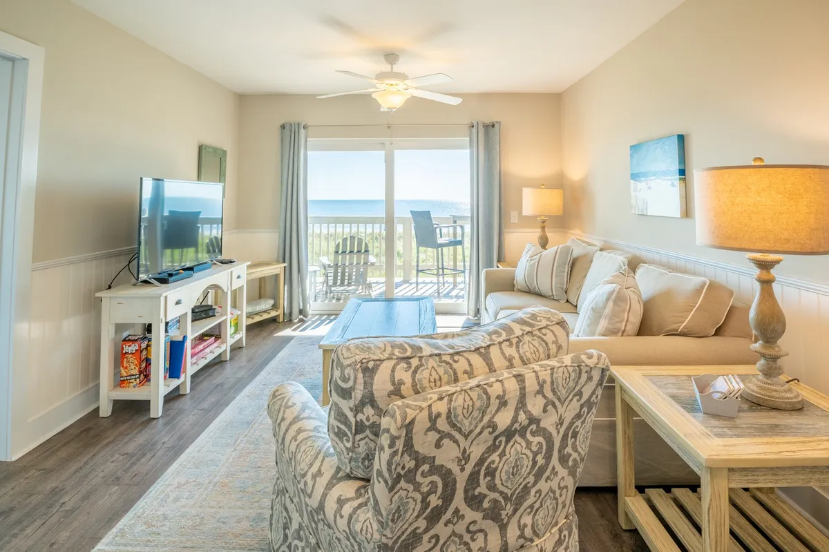 A comfortable seating area with soft furnishings, a large TV, and expansive windows framing an ocean view. The space is arranged for relaxation and entertainment, with plenty of natural light and a cozy atmosphere for family time.