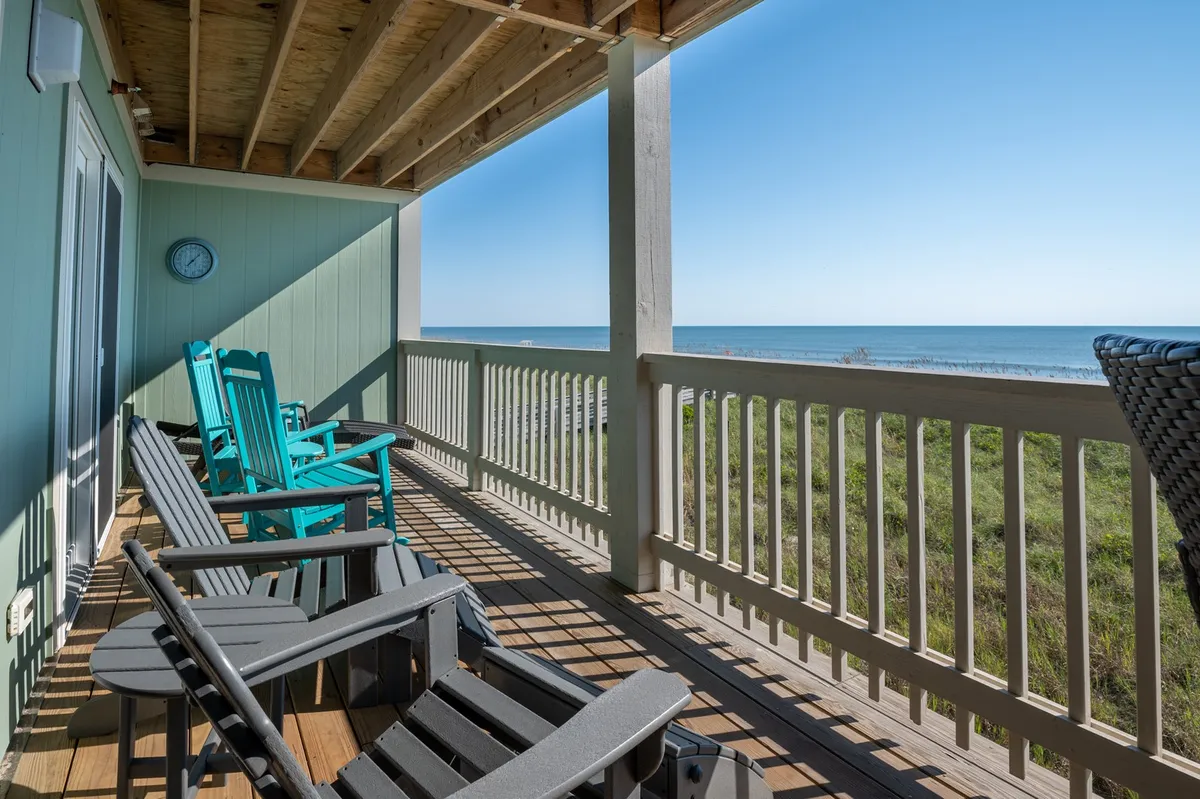 This image features a wooden oceanfront deck furnished with classic rocking chairs, all facing a sweeping view of the ocean. The tranquil ambiance is enhanced by the soothing expanse of water and the gentle glow of sunrise or sunset. The deck's inviting setup encourages relaxation and ocean gazing.