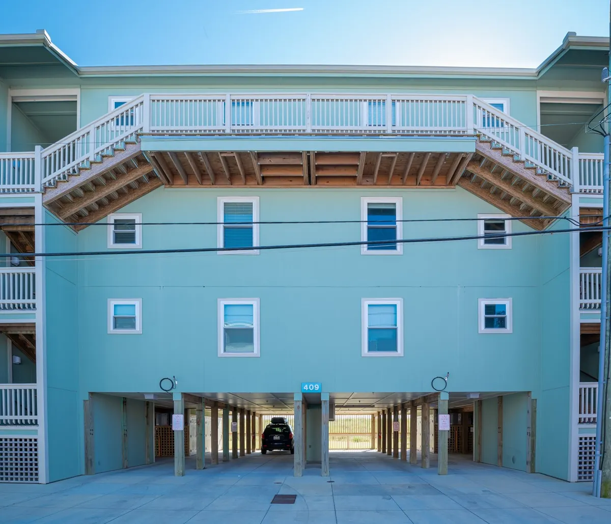 The elevated deck of the property is shown from the exterior, revealing the green facade and numbered entrance (409). The deck offers outdoor seating, and the surroundings suggest a casual, welcoming environment ideal for gathering and enjoying fresh air.