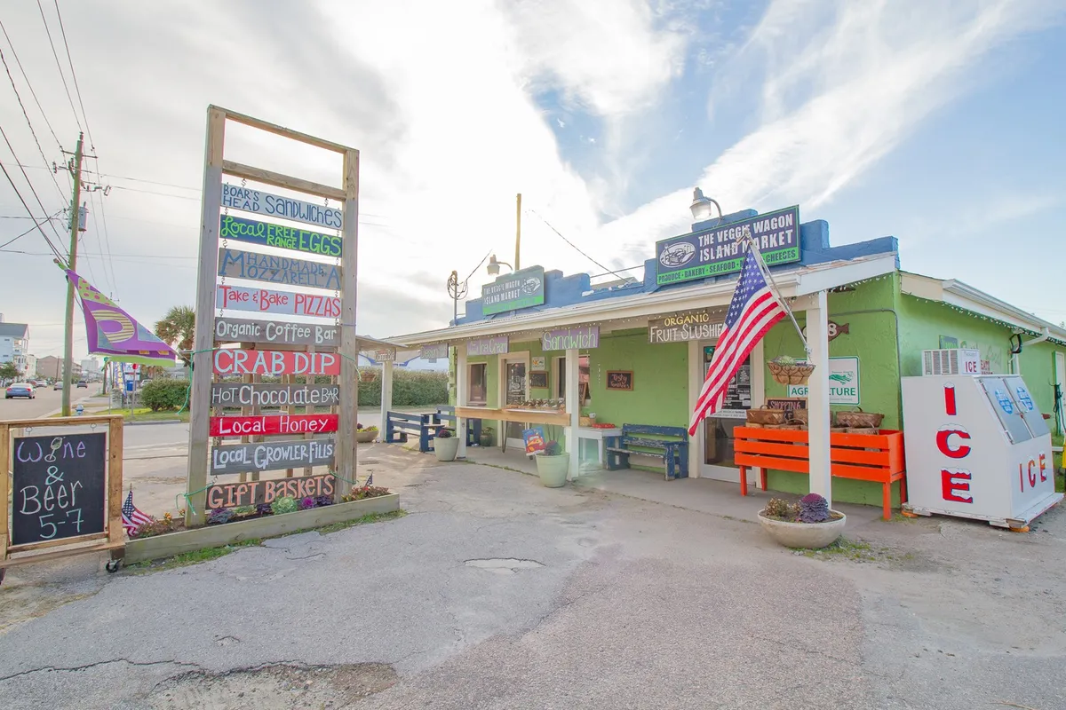 The photo showcases a bustling open-air market with colorful signboards, an American flag, and multiple market stalls. People are engaging in friendly exchanges, shopping for local produce, and enjoying the vibrant community atmosphere.
