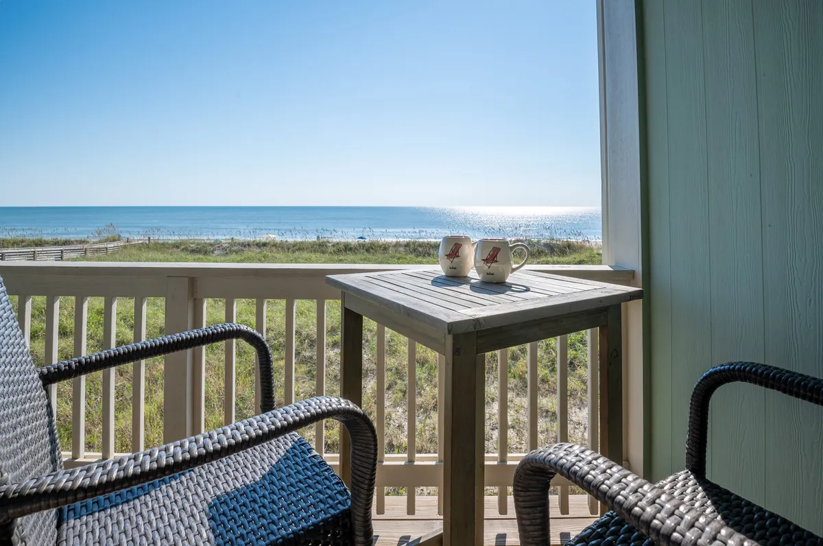 A peaceful moment is captured here, with two coffee mugs resting on an outdoor deck table, cushioned seating, and an expansive ocean view. The image exudes tranquility and suggests leisurely mornings spent enjoying coffee while listening to the sounds of the sea.